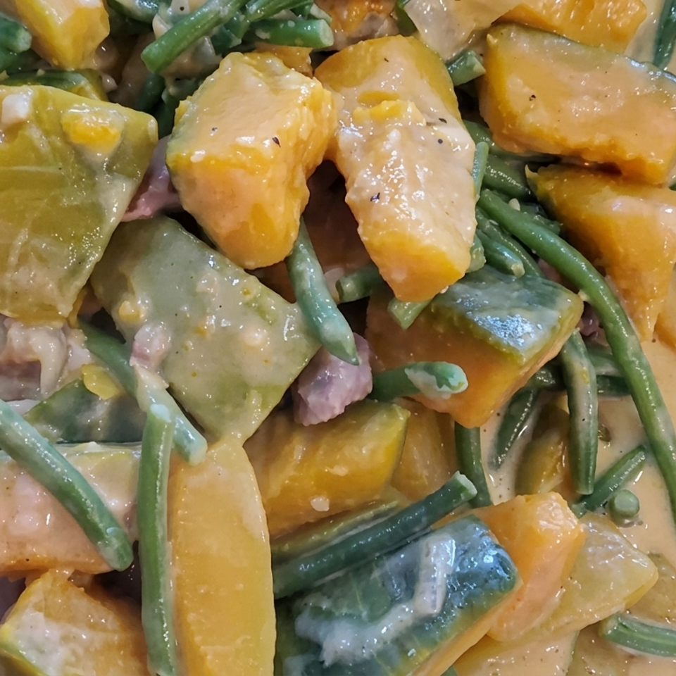 Creamy vegetable curry with green beans, squash, pumpkin, and chunks of meat in a serving tray.