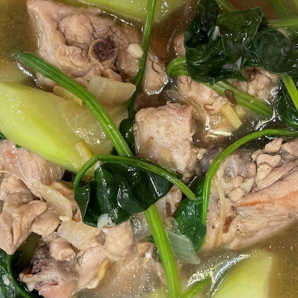 Clear soup with bone-in chicken pieces, leafy greens, pale vegetables, and herbs in a white bowl.